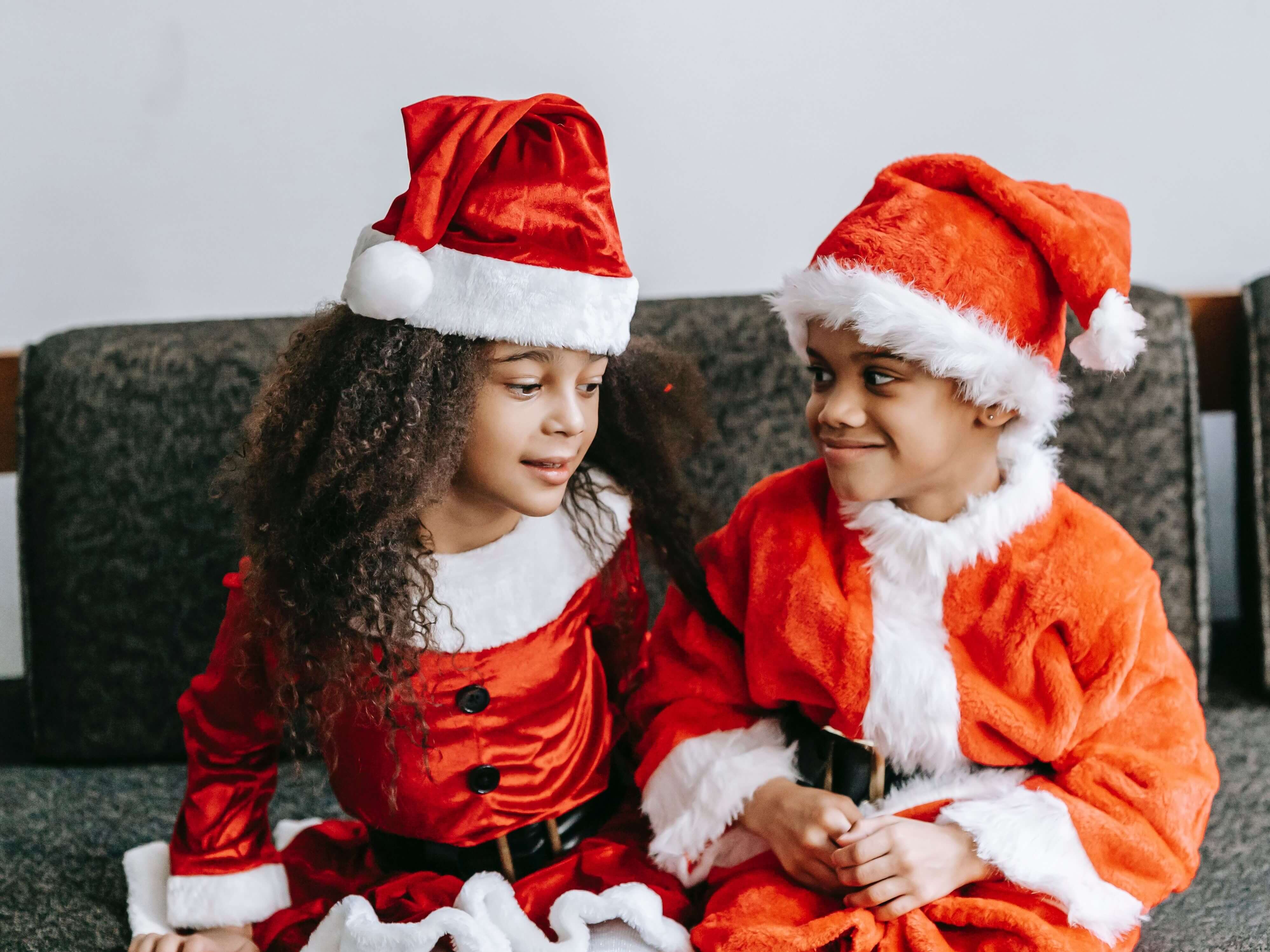 two children dressed in santa suits sitting on a couch