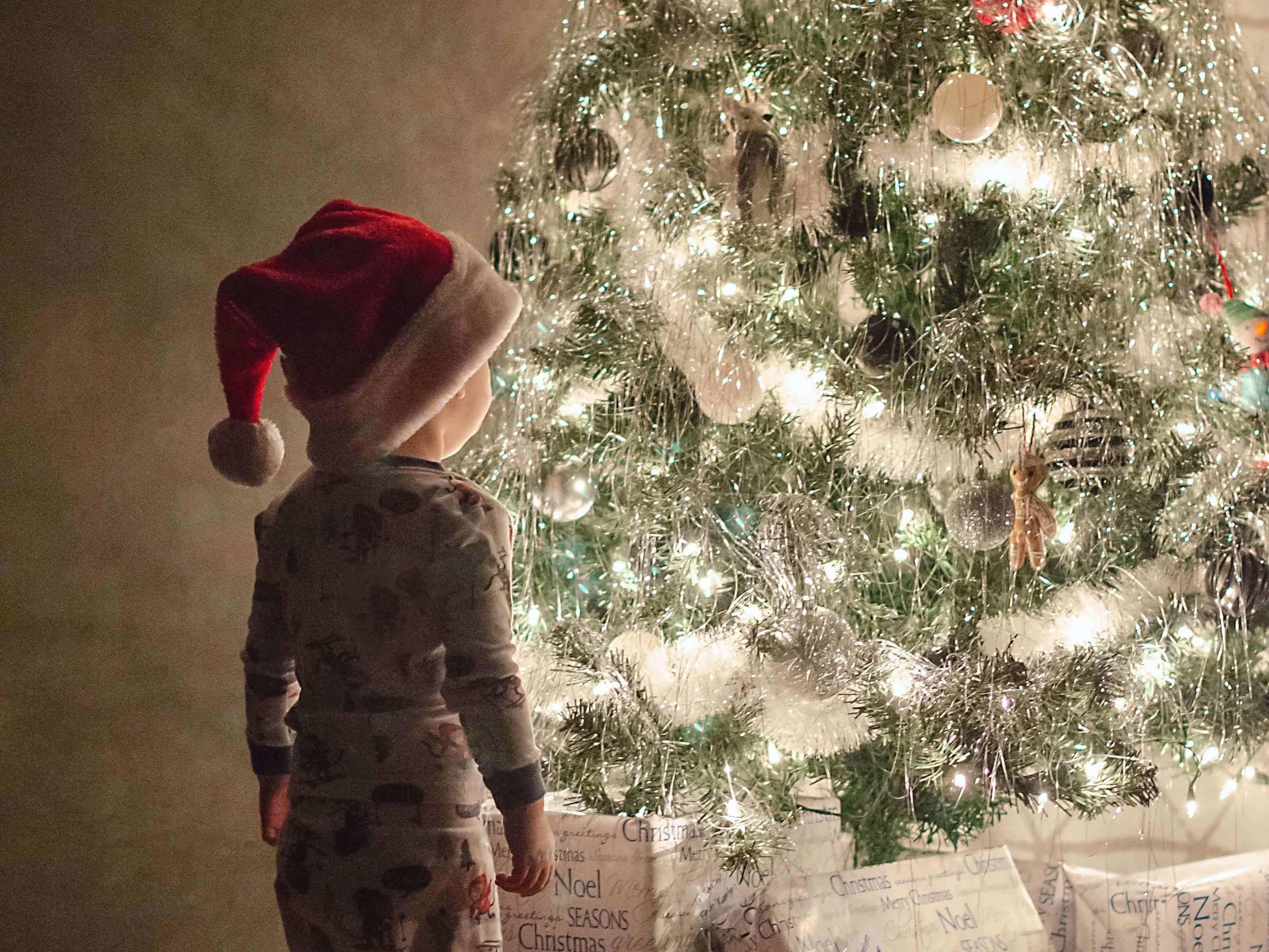 A young child stands in front of a lit christmas tree